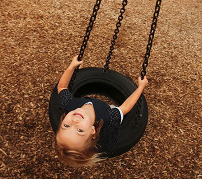 A child on a tire swing in a park with a Fibertop surface
